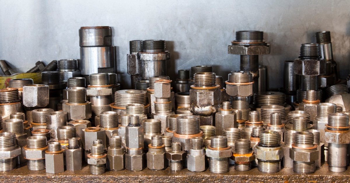 Several adapters for hydraulic hoses in different sizes and made of different materials sit on a surface.