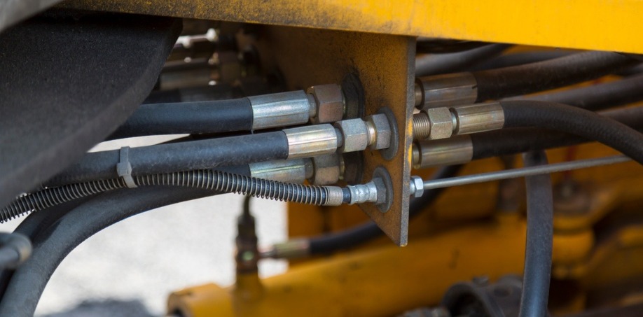 A close-up of a rusty and dirty hydraulic system, hoses, and other details of yellow road industrial machinery.