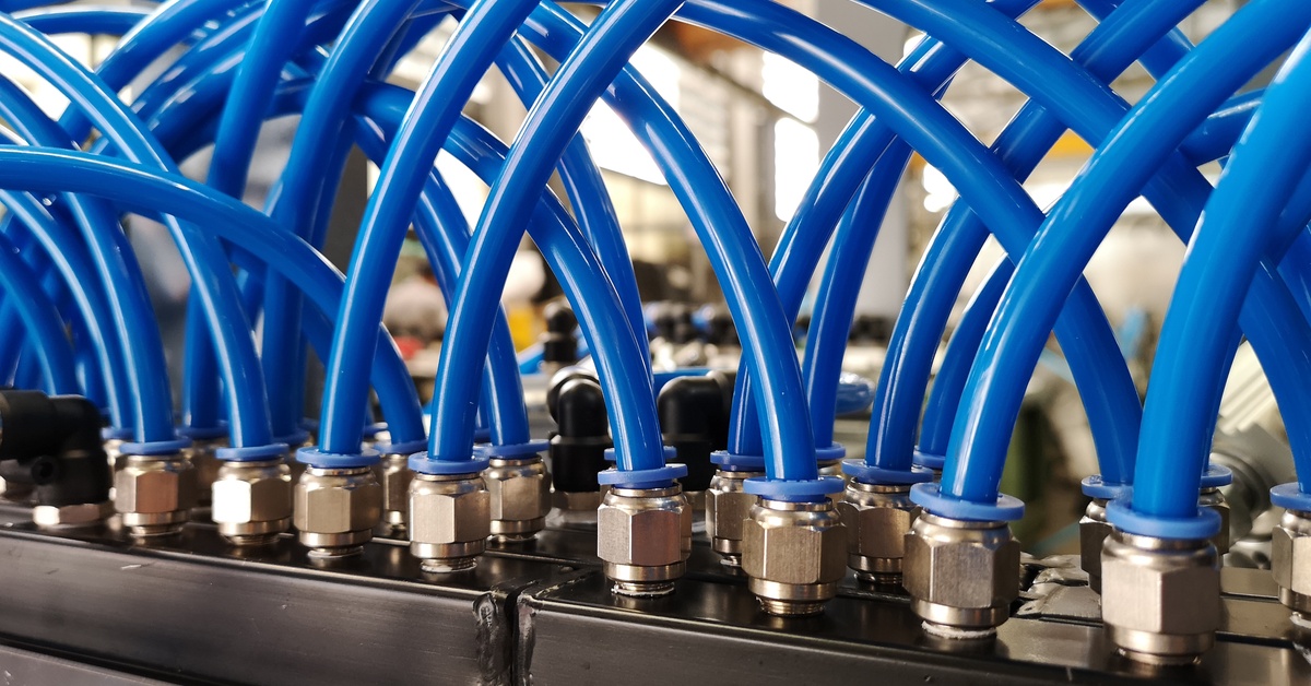 Blue hoses with pneumatic fittings on them are connected to black industrial equipment. The background is blurred.