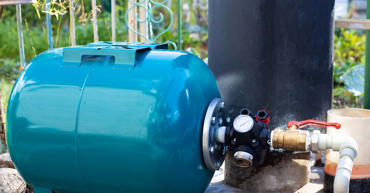 A close-up of a blue water supply system with a hydraulic tank and a cleaning filter from a well in the country.