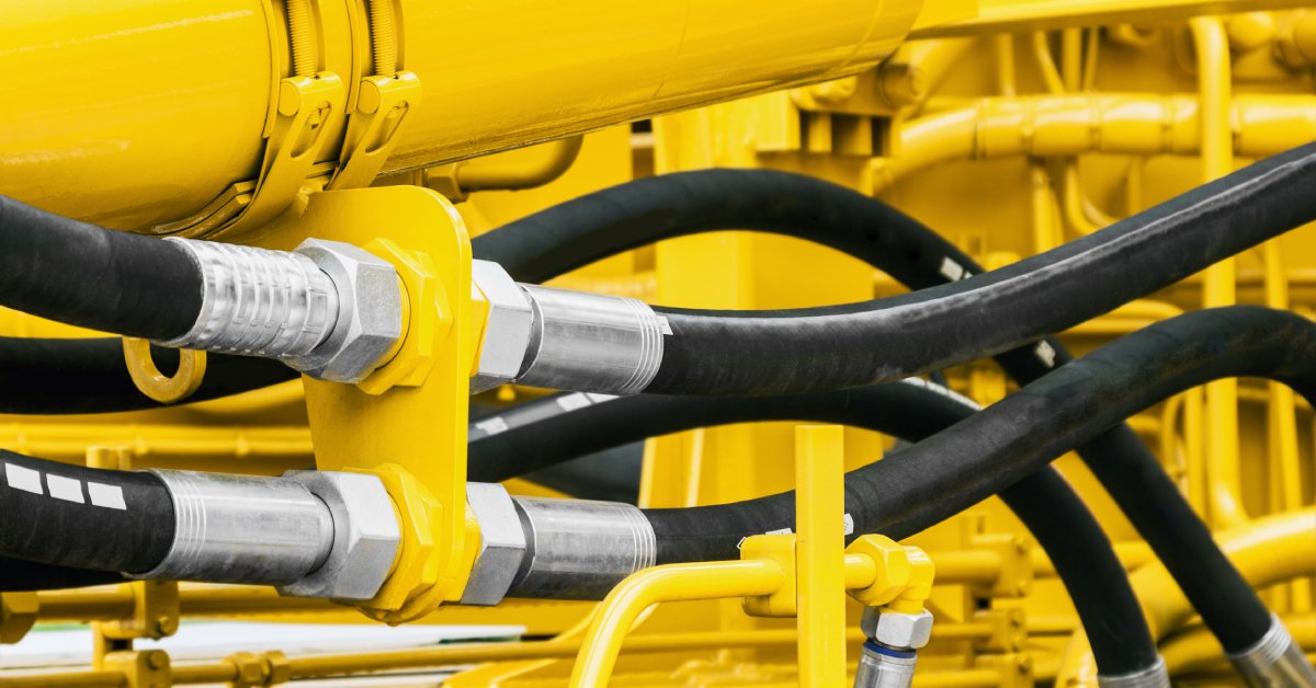 A close-up of bright yellow construction equipment. A few large hydraulic hoses are running through the equipment.