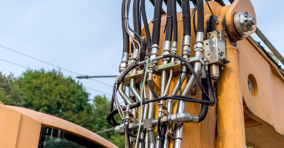 A close-up of the top half of an excavator where several hydraulic hoses are positioned. The hoses are connected to metal piping.