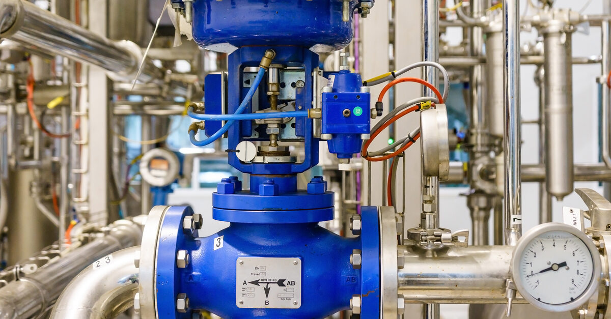 A close-up of a blue painted pneumatic control valve in a steam-heating system. It's surrounded by silver pipes, some with gauges.