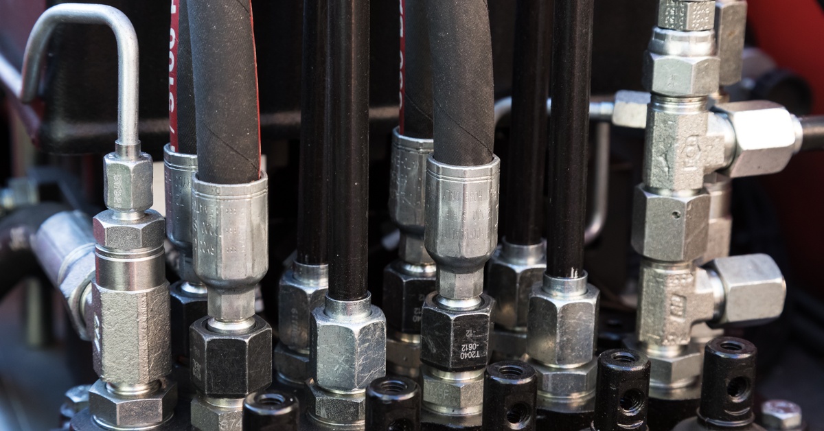 Hydraulic hoses, metal couplings, connectors, and fittings on a heavy-duty industrial machine.