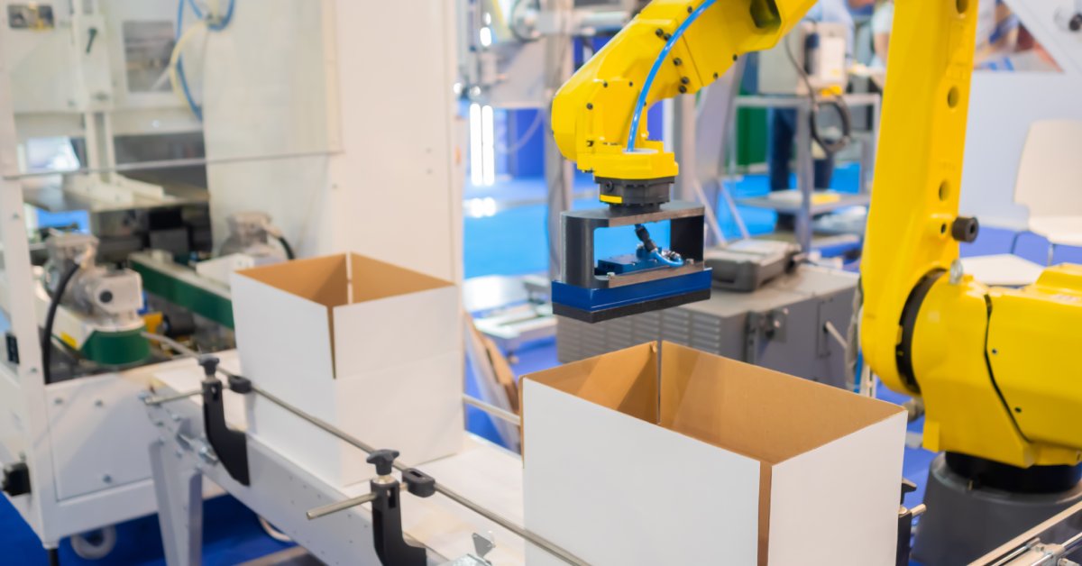 A yellow robotic arm used in an automatic sorting conveyor system hovers over white cardboard boxes.