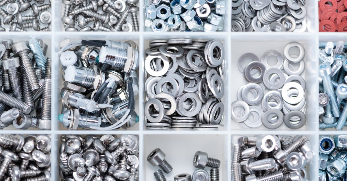 Industrial metal parts of varying shapes and sizes are sorted into different compartments in a plastic container.