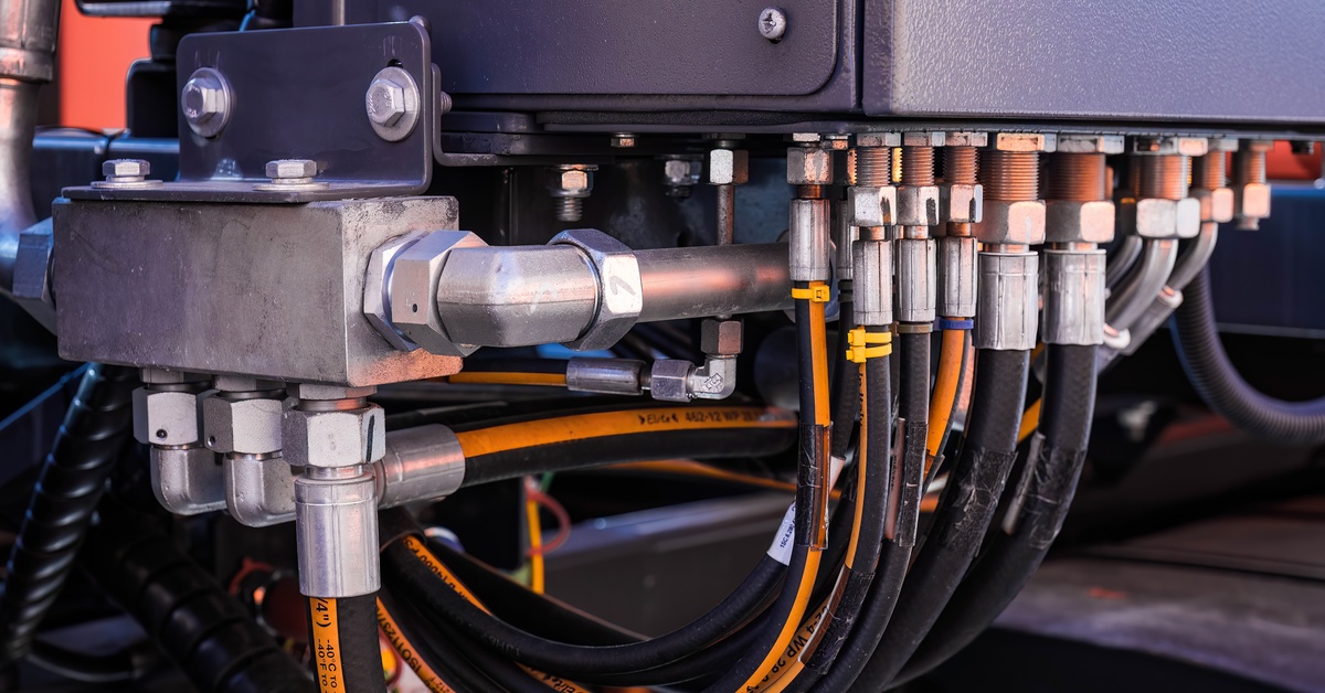Several hydraulic hoses and fittings are attached to an industrial oil system device inside a facility.