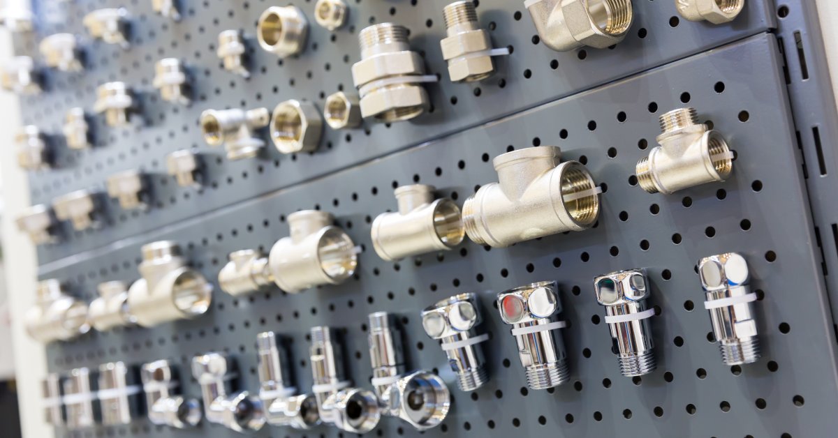 A set of industrial adapters, fittings, and other pipe fixture components displayed on a gray pegboard.