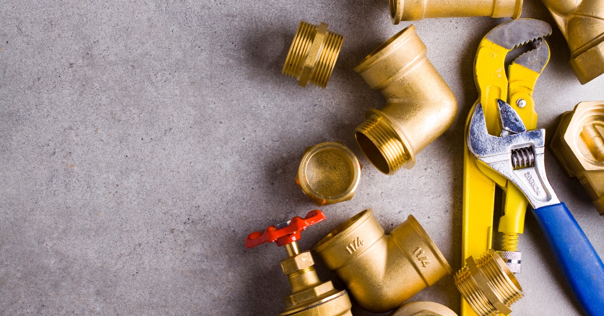 Brass fittings, threaded reducers, a wrench, and pliers sitting together against a plain gray background.