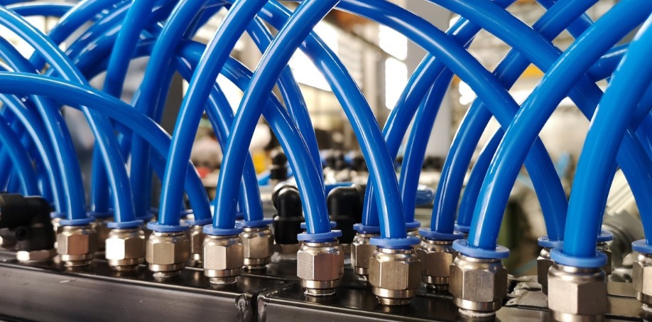 Dozens of pneumatic fittings connected to blue hoses for air or water installed on a black metal fixture.