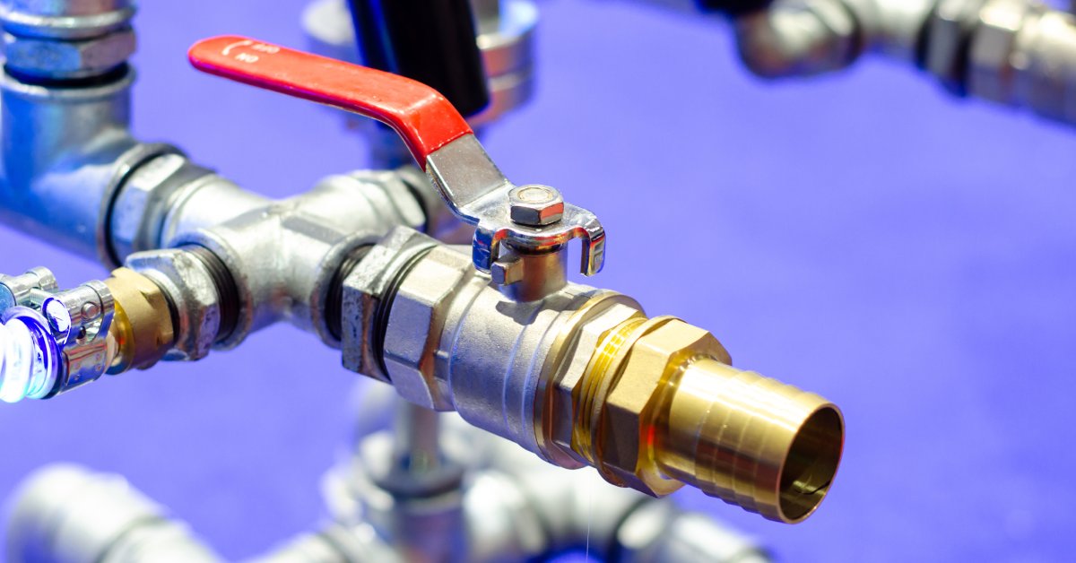 A close-up of silver and gold metal pipelines with ball valves in a warehouse setting, connected to other pipes.